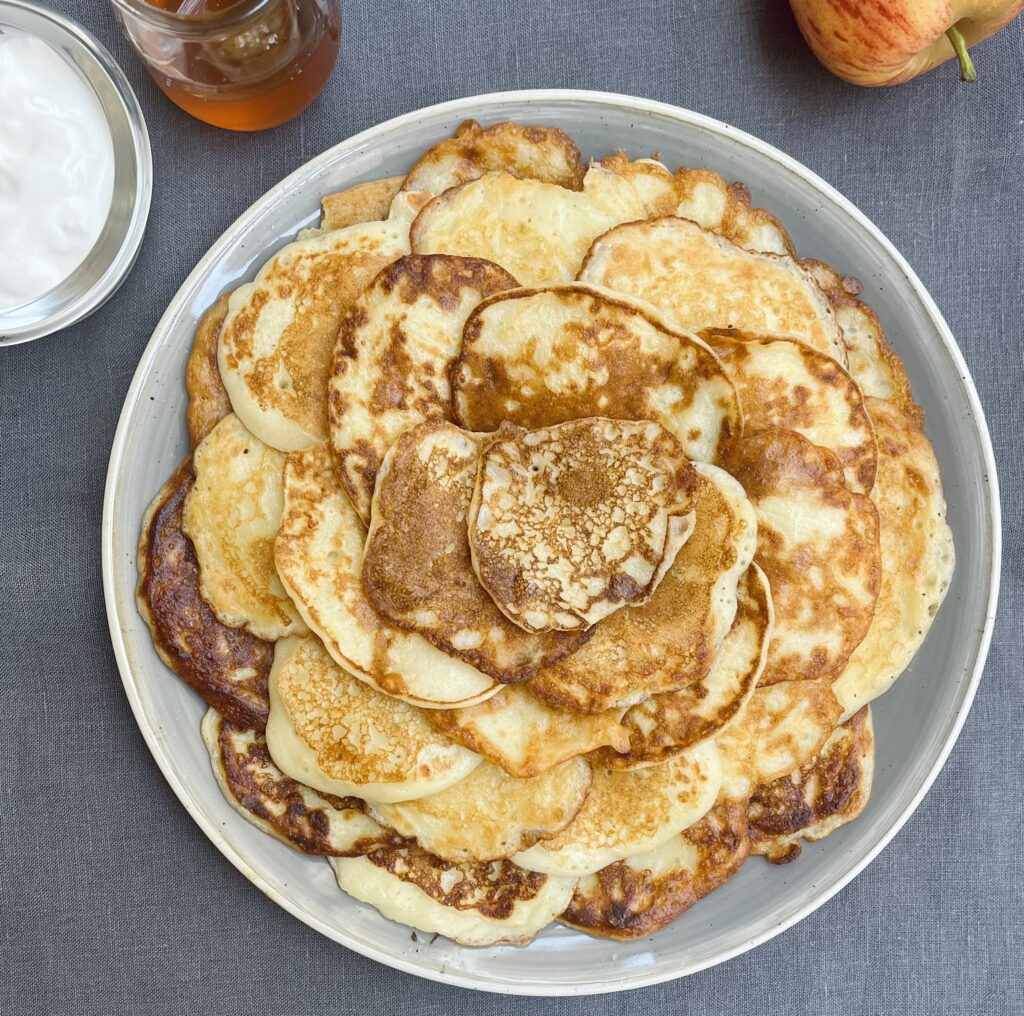 A neat pile of golden brown apple mini pancakes arrange on a light grey plate