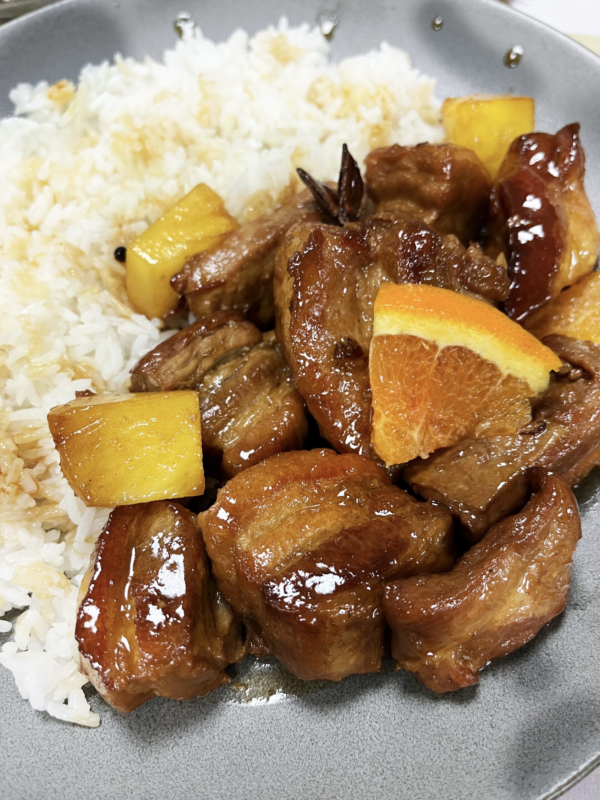 chunks of sticky pork belly are covered in a glossy glaze and topped with fresh pieces of orange and pineapple