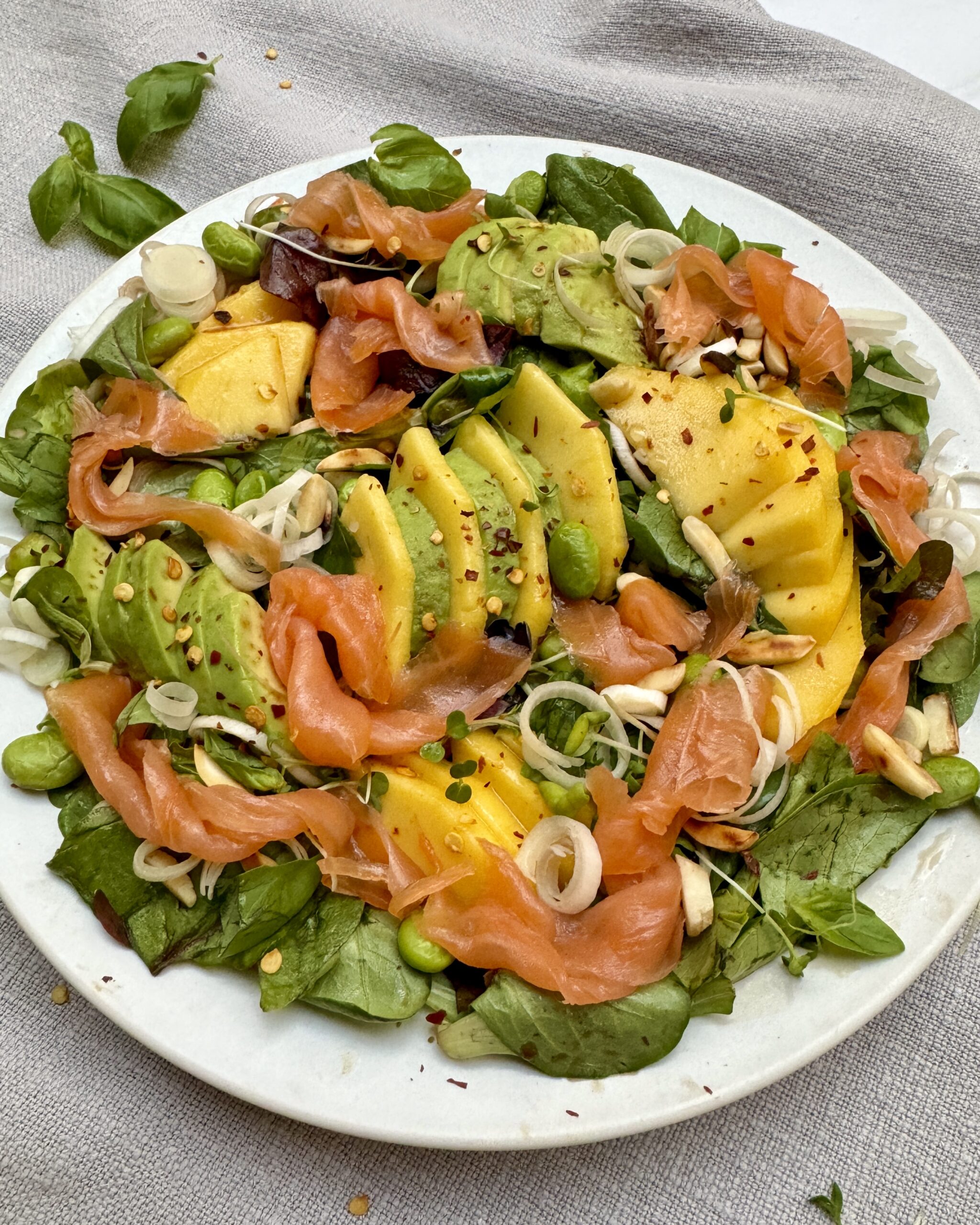 A plate of Smoked Salmon with Mango and Avocado, edamame, leeks and salad greens