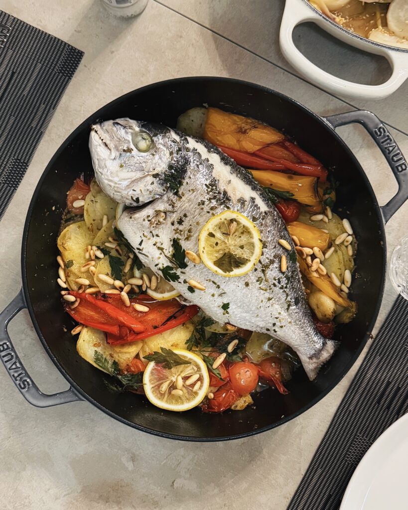 whole sea bream in a casserole with colorful vegetables, lemon and herbs