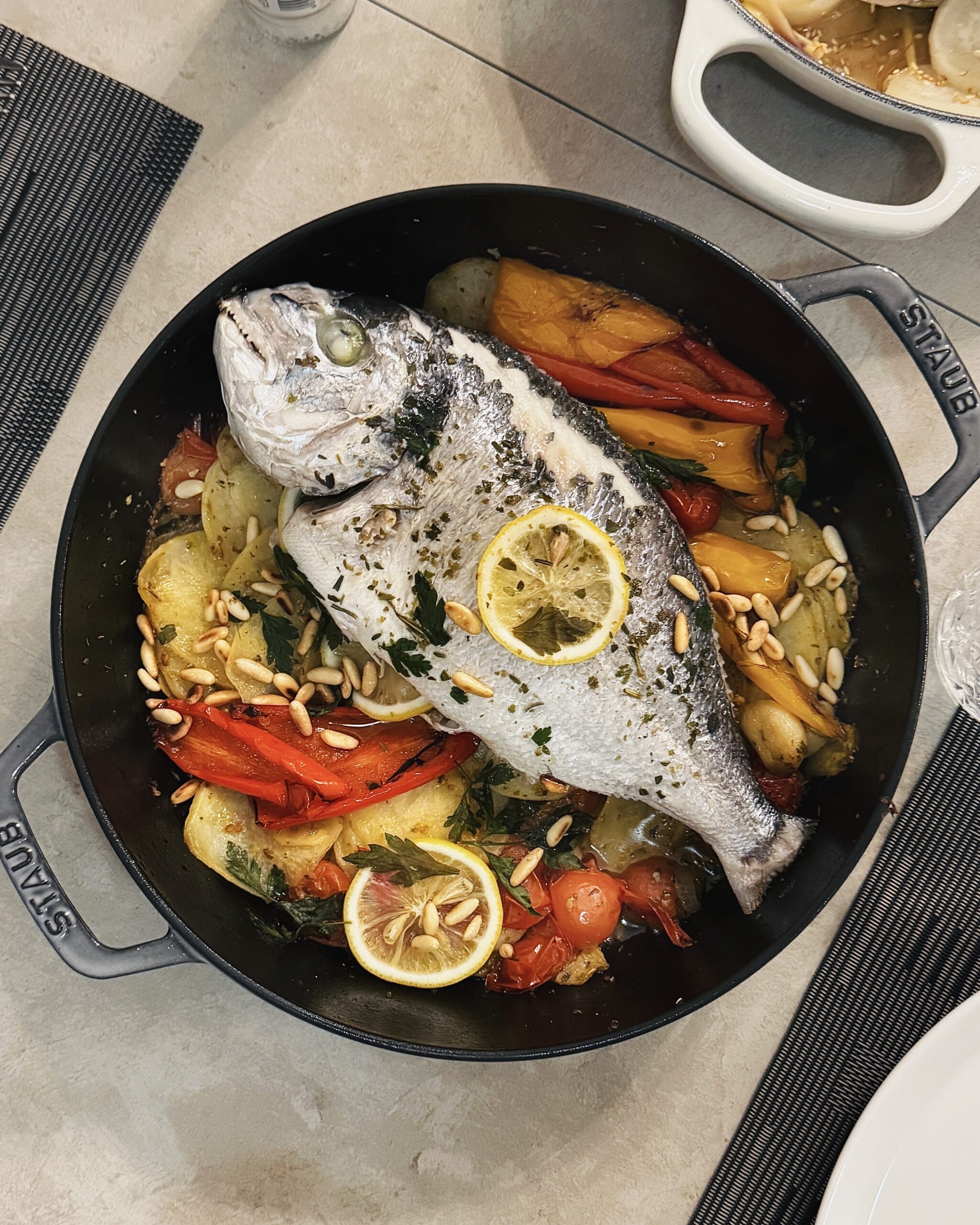 whole sea bream in a casserole with colorful vegetables, lemon and herbs