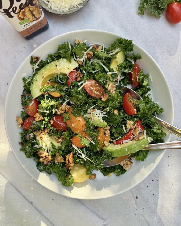 a plate with kale and avocado salad made with roasted bell peppers, cherry tomatoes, parmesan, walnuts