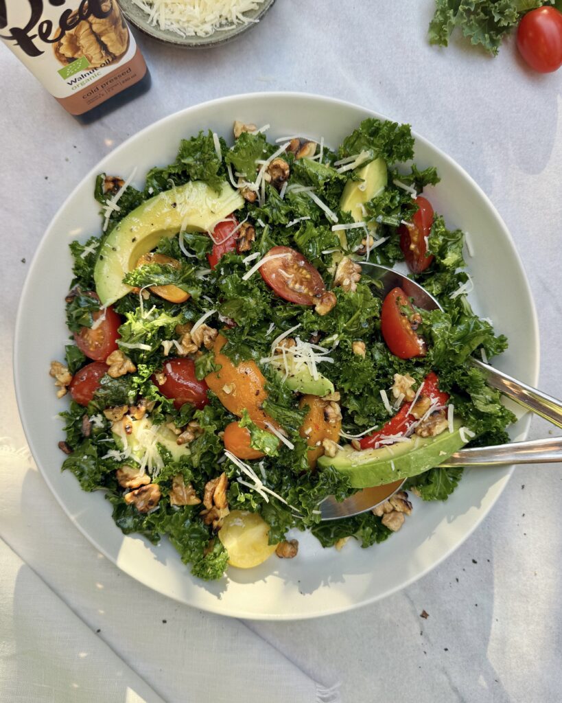 a plate with kale and avocado salad made with roasted bell peppers, cherry tomatoes, parmesan, walnuts