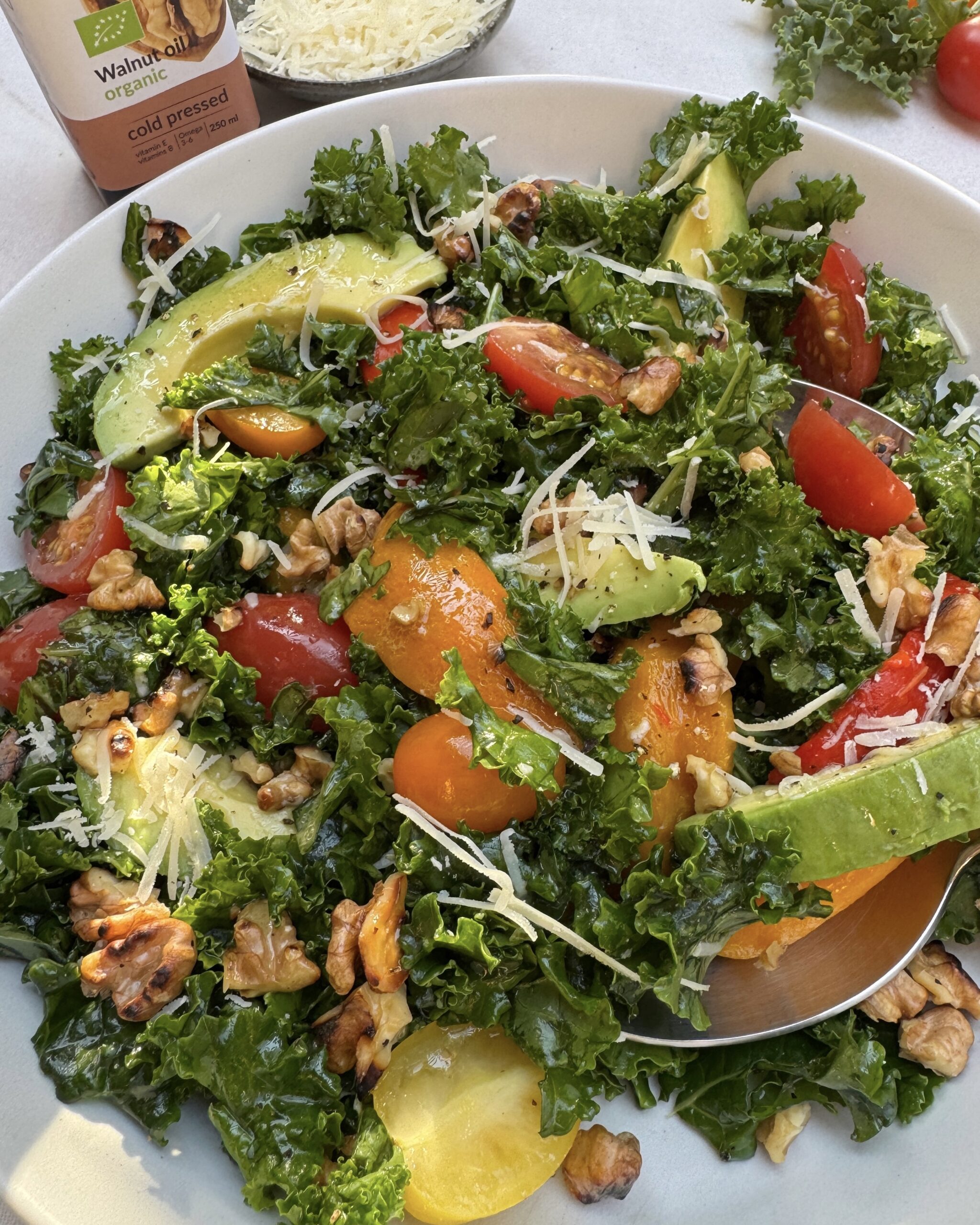 a close up on a plate with kale and avocado salad made with roasted bell peppers, cherry tomatoes, parmesan, walnuts