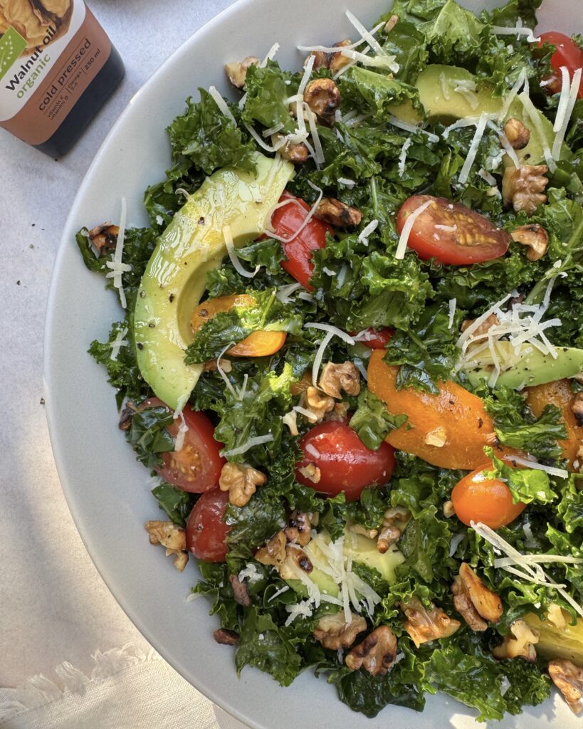 a close up on a plate with kale and avocado salad made with roasted bell peppers, cherry tomatoes, parmesan, walnuts