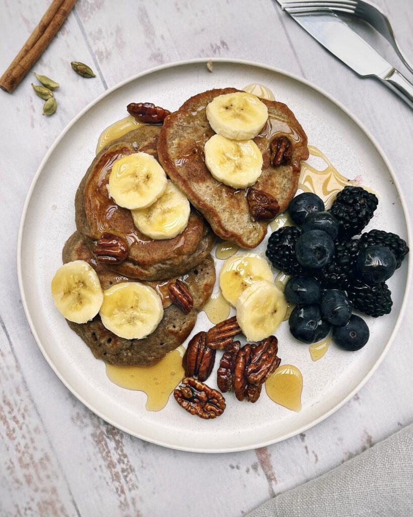 a plate with fluffy banana pancakes topped with honey and banana slices and served with berries