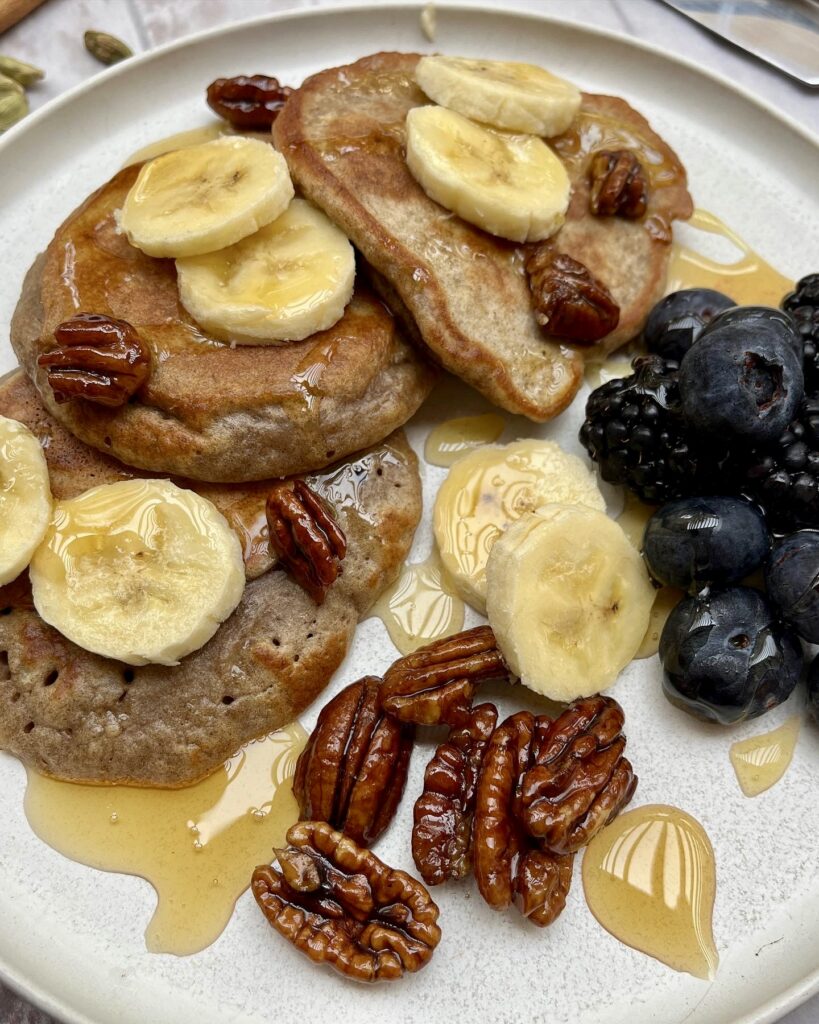 a plate with fluffy banana pancakes topped with honey and banana slices and served with berries