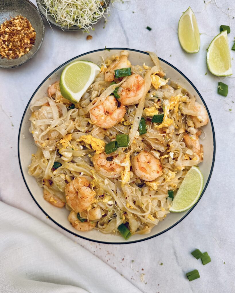 a plate with pad thai, rice noodles with prawns, egg, lime and pad thai sauce