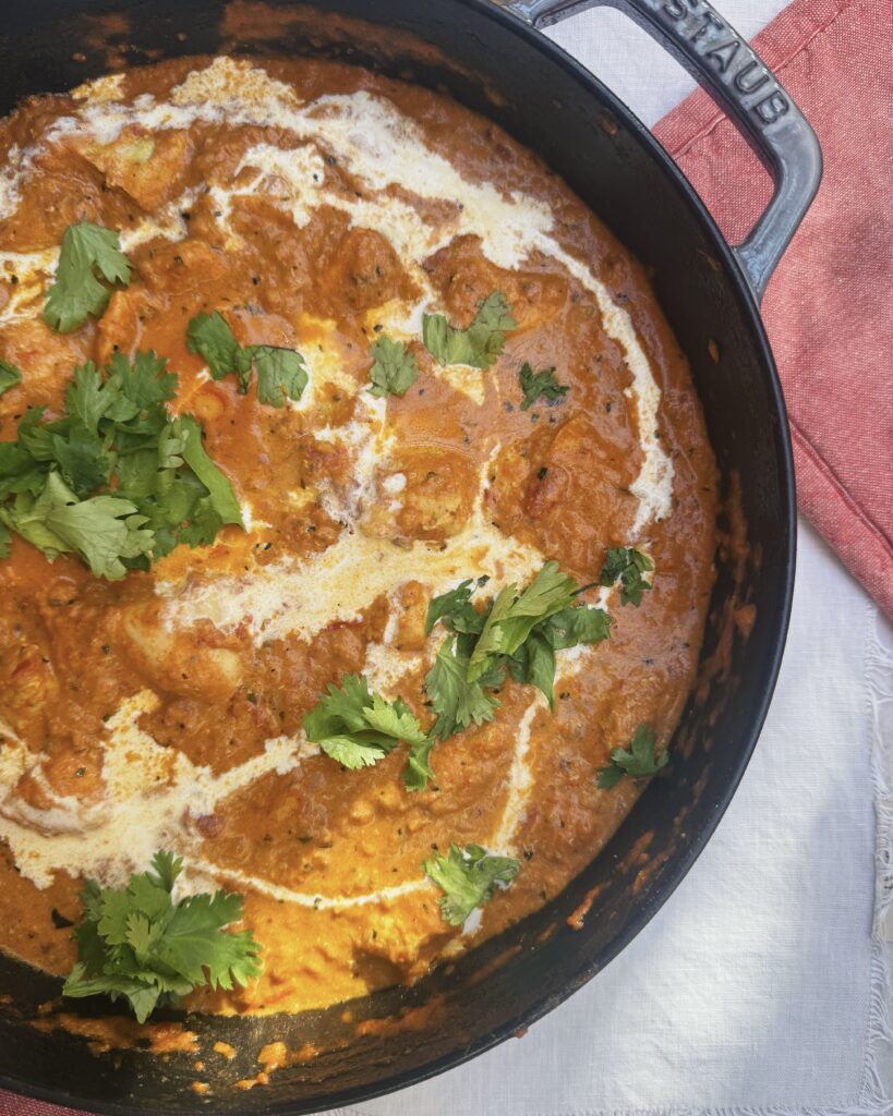 a pot with chicken tikka masala garnished with cream and cilantro