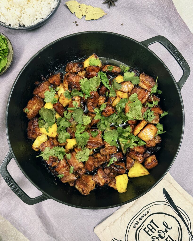 a casserole with pork belly chunks in orange and pineapple glaze, garnished with fresh pineapple and cilantro